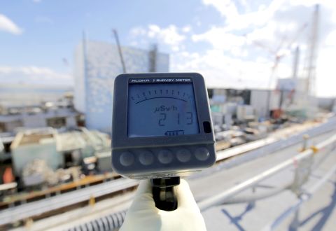 A TEPCO employee measures a radiation level of 213 microsieverts per hour in front of the No. 2, left, and No. 3 reactor buildings on February 10.