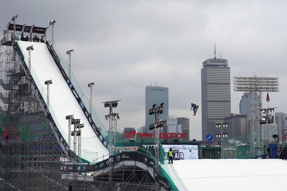 A snowboarder is captured making a jump with the high rise buildings of central Boston in the background.