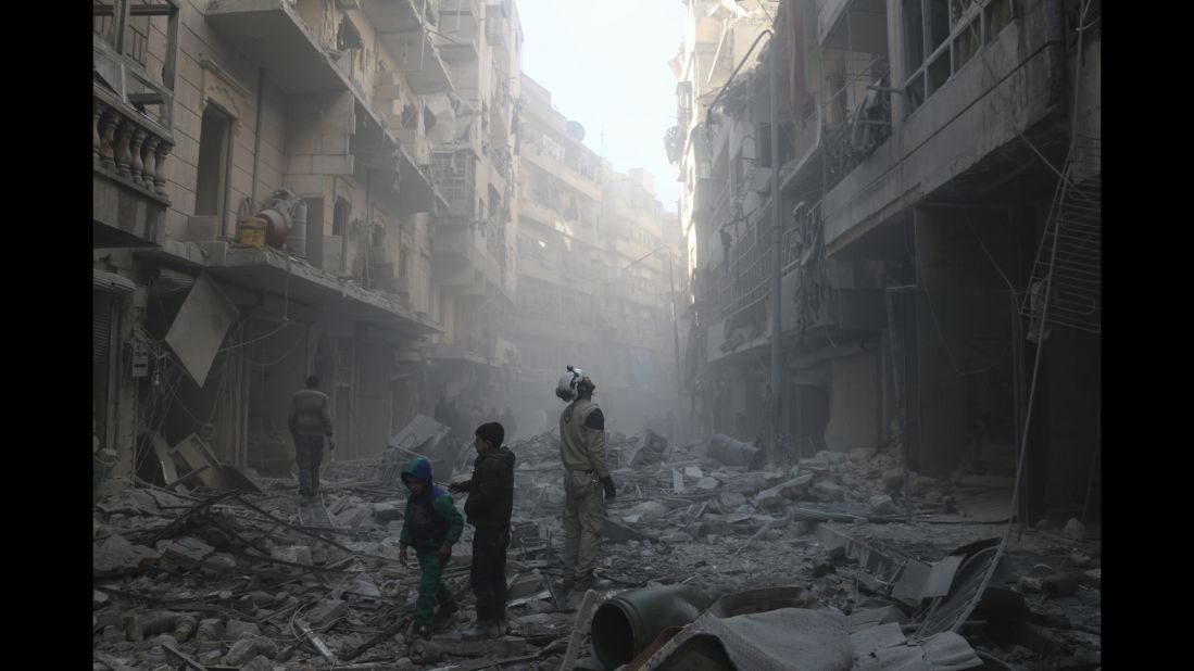 Two children walk past a "White Helmet" soon after an airstrike hits the Shaar neighborhood of Aleppo.