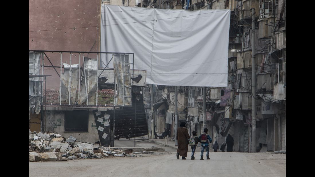 A mother watches over her children as they return from school; the massive sheet hanging in the street is to deter government snipers.