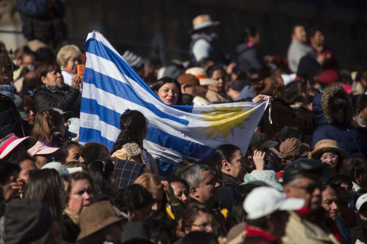 A woman holds an Uruguayan flag while she waits along the route that Pope Francis would take to Mexico City's main square.