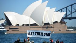 Members of the environmental group Greenpeace hold up a sign that reads "#LET THEM STAY" in front of the Opera House in Sydney on February 14, 2016.  An Australian hospital in Brisbane has refused to send an asylum-seeker baby back to detention in Nauru as momentum builds across the country against offshore Pacific camps for used by the Australia government for processing refugees who try to get to Australia. AFP PHOTO / Peter PARKS / AFP / PETER PARKS        (Photo credit should read PETER PARKS/AFP/Getty Images)