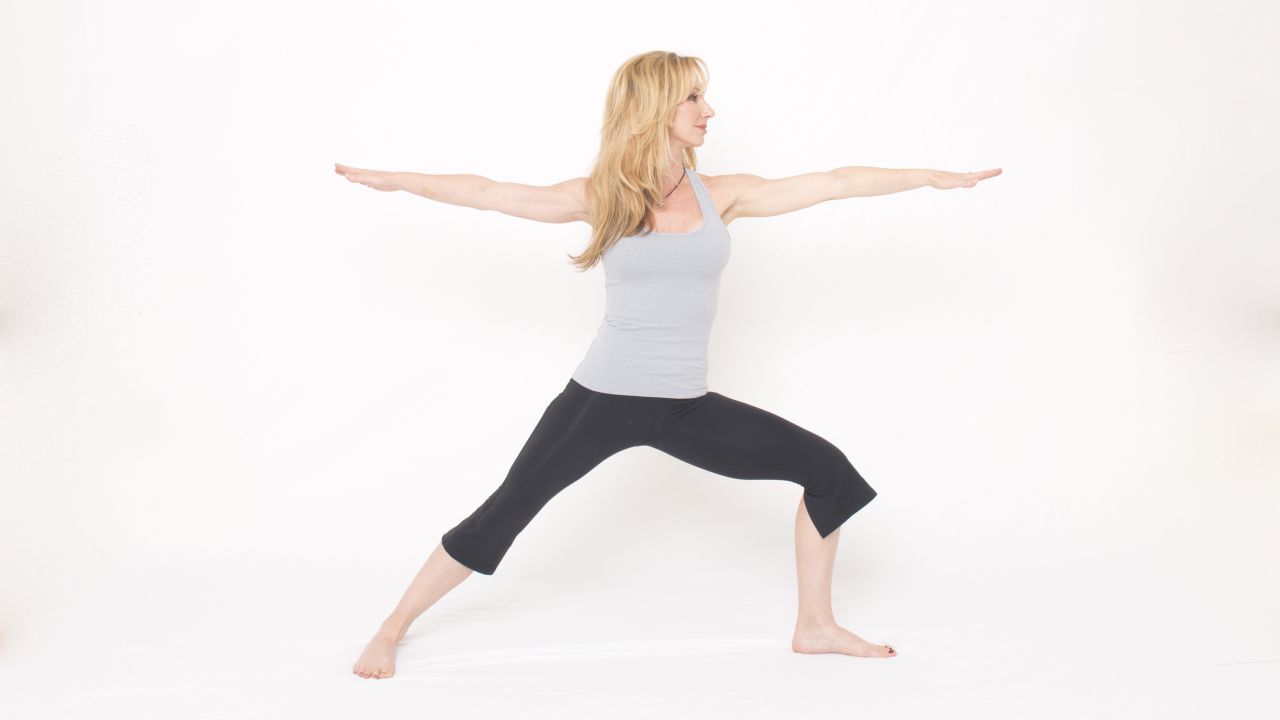 From warrior one pose, open your right hip to angle your right foot out to 90 degrees. Maintain the muscular effort from the previous pose to keep your right leg straight and your left knee bent above your ankle. Do not allow the knee to dip inward and come out of alignment with the ankle. Open your upper body to the right as you bring your arms down to shoulder height and out to the sides, aligned over your hips. Reach your right arm back and left arm forward with your palms down.