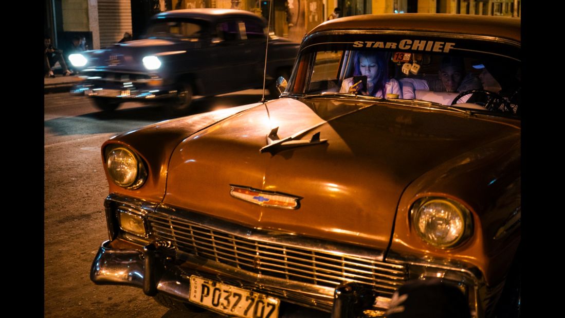 A young woman in Havana uses her phone in an old Chevrolet.