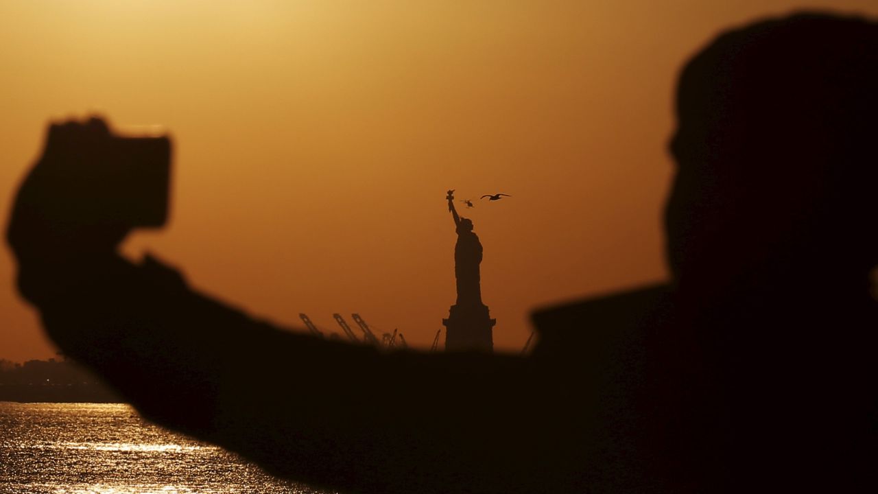 The Statue of Liberty is seen in the background while a couple poses for a selfie in New York on Saturday, February 20.