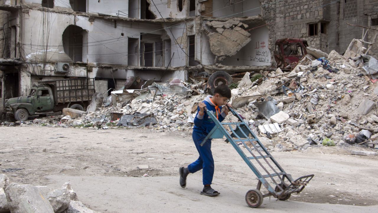 A boy walks a hand truck through a heavily damaged area in Aleppo. 