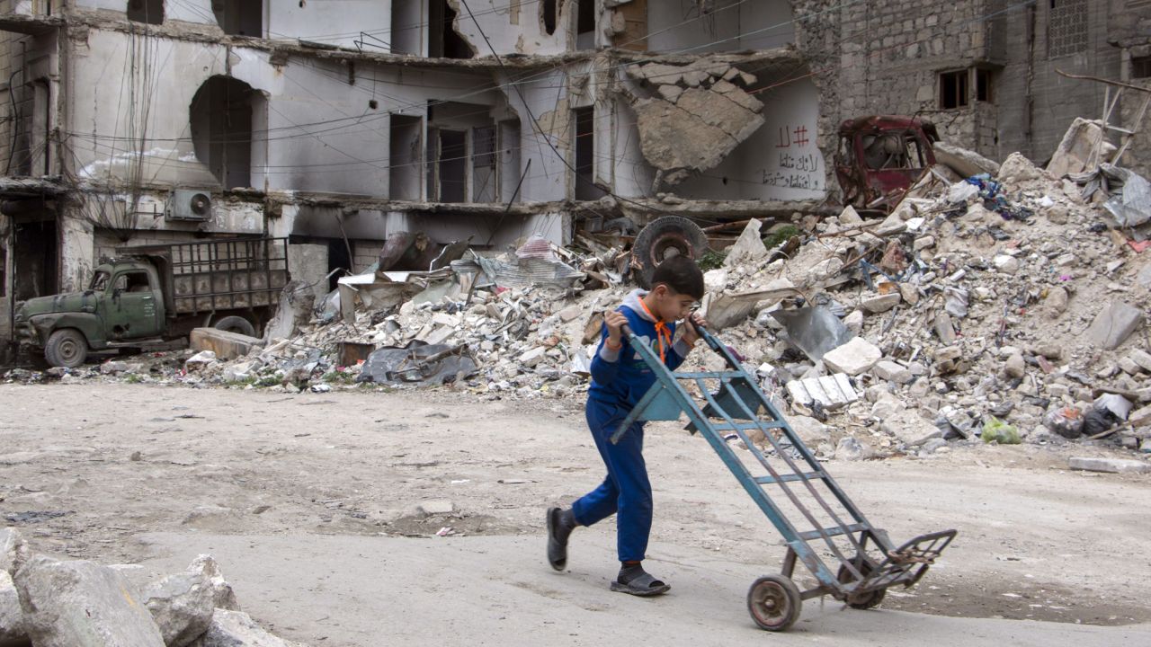 A boy walks a hand truck through a heavily damaged area in Aleppo.