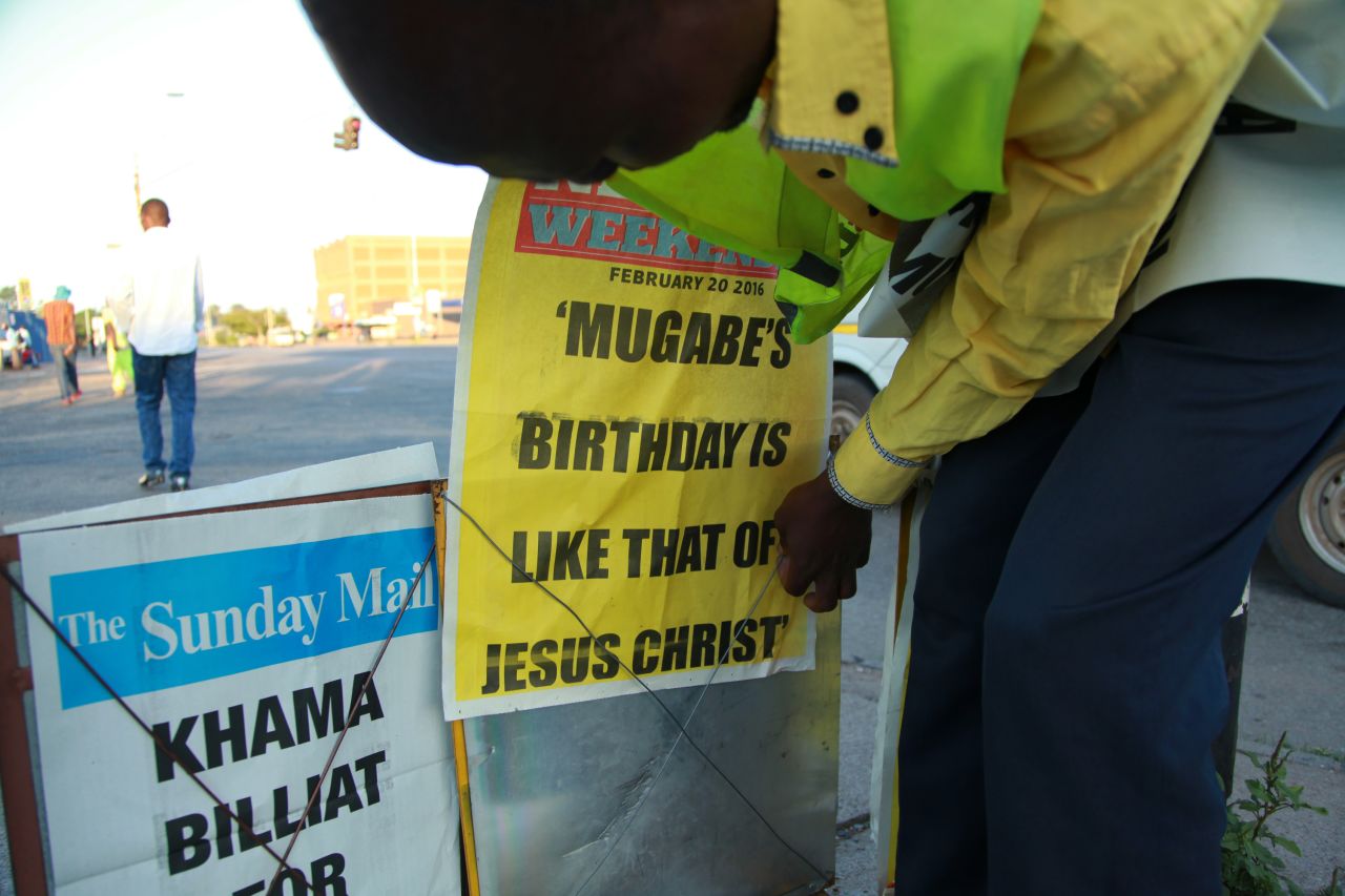 A newspaper vendor in Harare places a banner describing  Zimbabwean President Robert Mugabe's birthday as being like that of Jesus Christ, on Sunday, February 21, 2016. 
