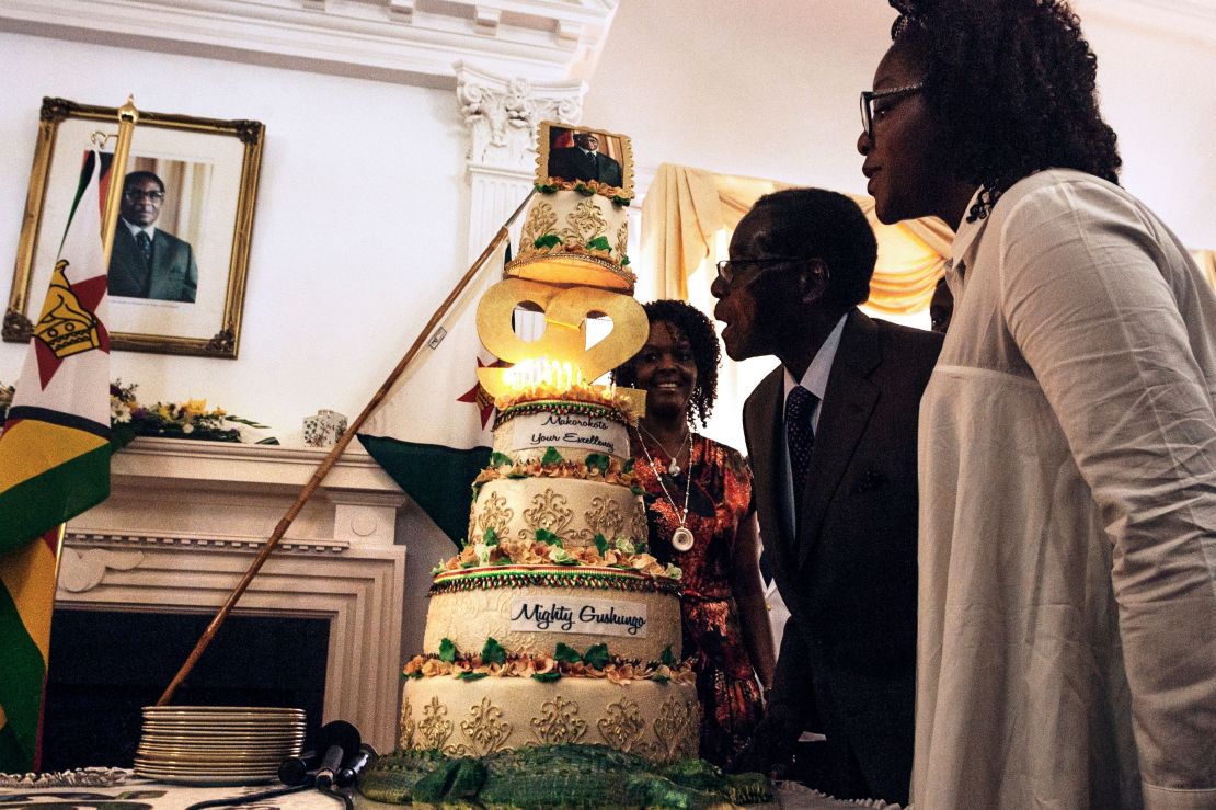 Zimbabwe President Robert Mugabe (C), flanked by his wife Grace Mugabe (L) and daughter Bona (R), blows out the candles on a cake celebrating his 92nd birthday.