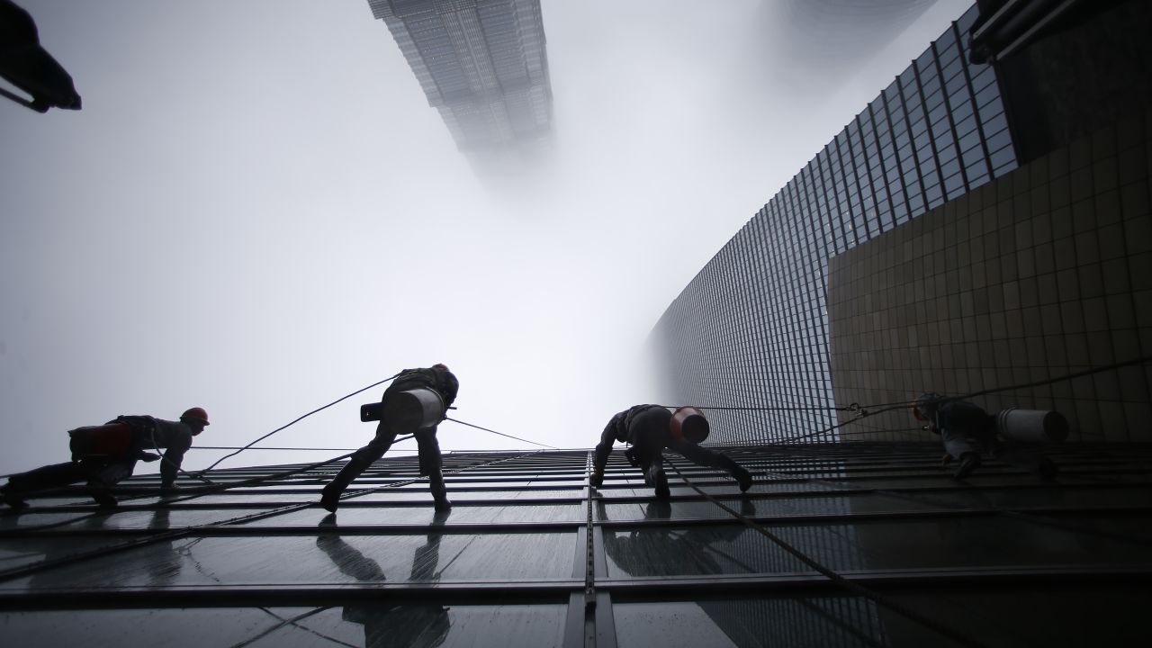 Workers clean the Shanghai World Financial Center in the financial district of Pudong. Shanghai Tower is seen at the top of the picture, and Jin Mao Tower is to the left.