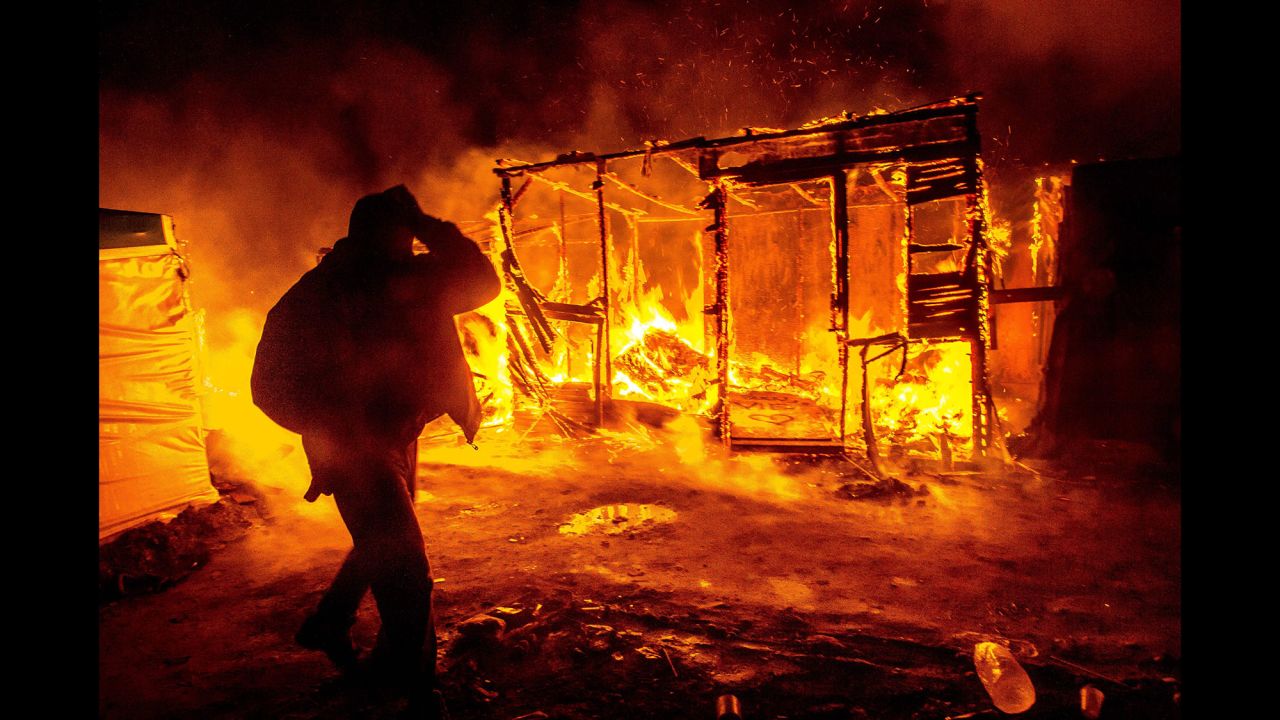 A migrant walks past a burning shack in the southern part of the 