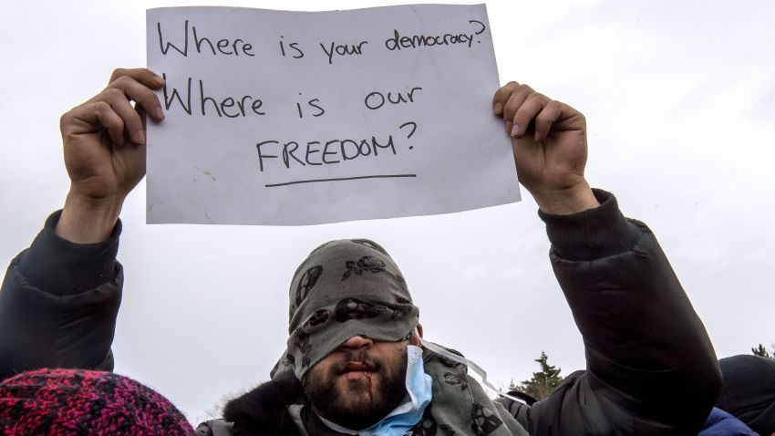 TOPSHOT - An Iranian migrant with sewn lips, holds a placard reading "where is your democracy? where is our freedom?", as he demonstrates during the demolition of the southern part of the so-called "Jungle" migrant camp, on March 2, 2016, in Calais.
French demolition workers set about razing makeshift shelters in the "Jungle" migrant camp for a third day on March 2, 2016 under close watch of dozens of police officers equipped with water cannon. The destruction of the southern half of the sprawling shantytown in the northern port city of Calais, where thousands of migrants and refugees have gathered in the hope of finding passage to England, has sparked often violent resistance from residents. / AFP / PHILIPPE HUGUEN        (Photo credit should read PHILIPPE HUGUEN/AFP/Getty Images)