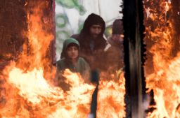 Migrants watch burning shacks in the southern part of the so-called 'Jungle' migrant camp, on March 2, 2016 in Calais, northern France.