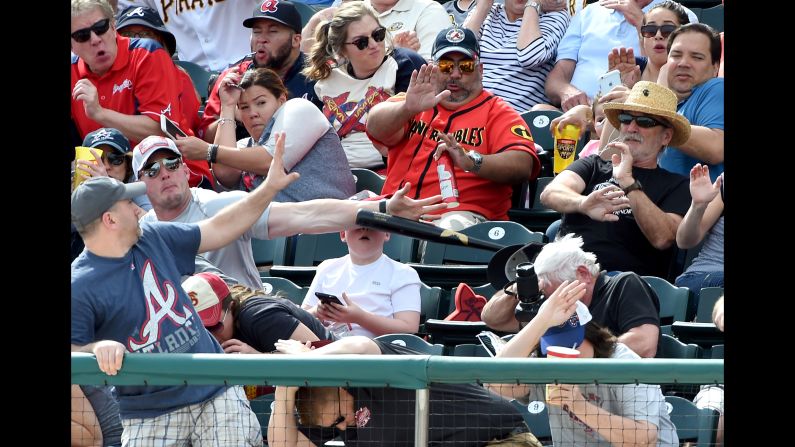A man knocks down a baseball bat that flew into the stands during a spring-training game in Lake Buena Vista, Florida, on Saturday, March 5. The bat was heading toward a young boy who was looking at a cell phone.