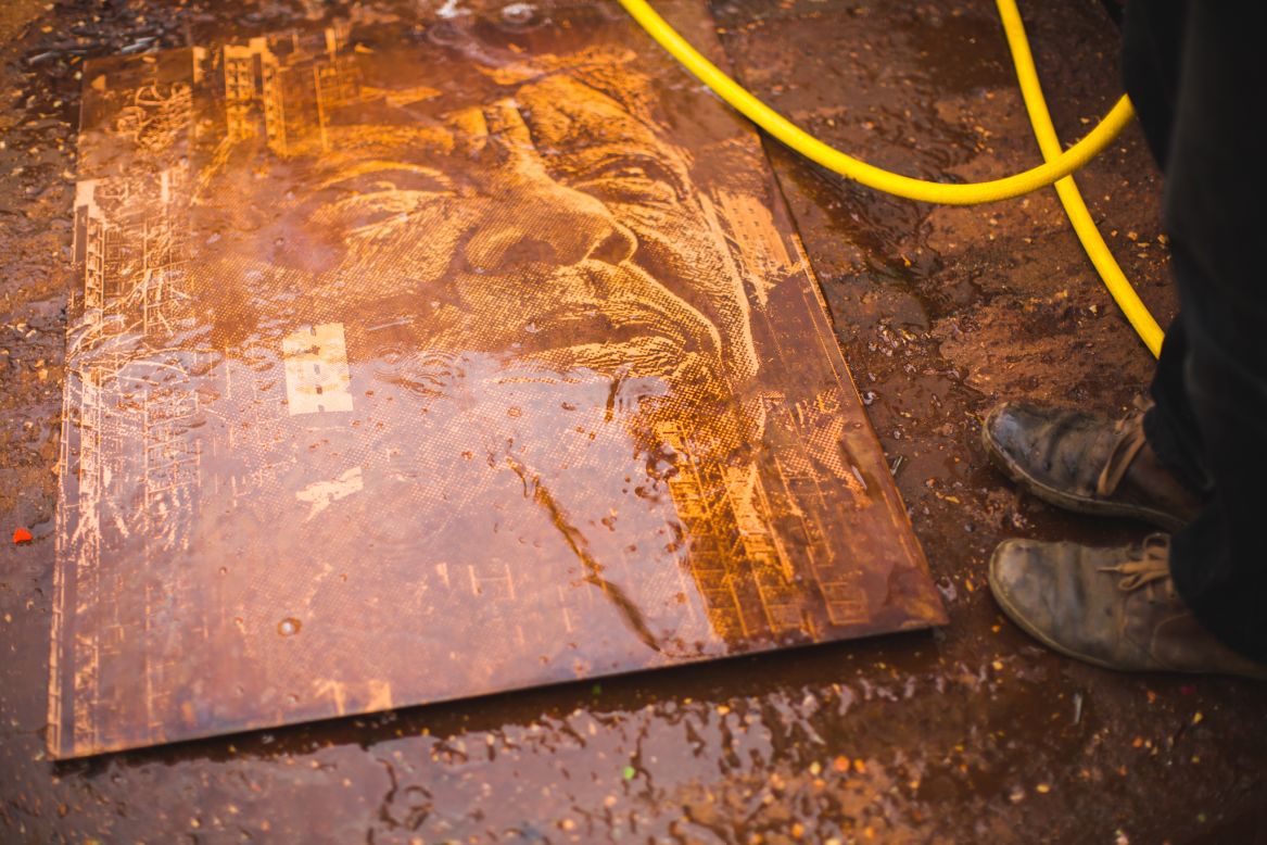 An etched metal plate being washed after an acid bath. 