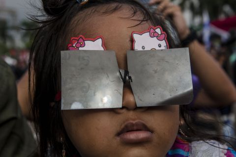A young girl in Palembang city wears a protective filter to shield her eyes while watching the eclipse. 