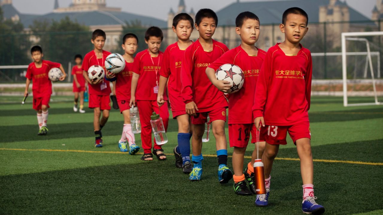 QINGYUAN, CHINA - JUNE 13:    Young Chinese football players walk to training at the Evergrande International Football School on June 13, 2014 near Qingyuan in Guangdong Province, China. The sprawling 167-acre campus is the brainchild of property tycoon Xu Jiayin, whose ambition is to train a generation of young athletes to establish China as a football powerhouse. The school is considered the largest football academy in the world with 2400 students, more than 50 pitches and a squad of Spanish coaches through a partnership with Real Madrid. (Photo by Kevin Frayer/Getty Images)