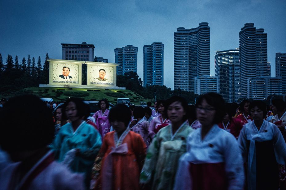 Women in traditional Korean dress head to the dance. Though much of North Korea is without electricity, the portraits of the supreme leaders are illuminated brightly. 