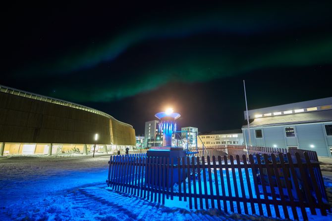 The northern lights flicker above the burning flame of the Arctic Winter Games in the center of Nuuk.
