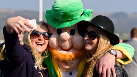 A man wearing a leprechaun fancy dress suit poses for a selfie during St Patrick's Day at the Cheltenham Festival at Cheltenham Racecourse on March 17, 2016