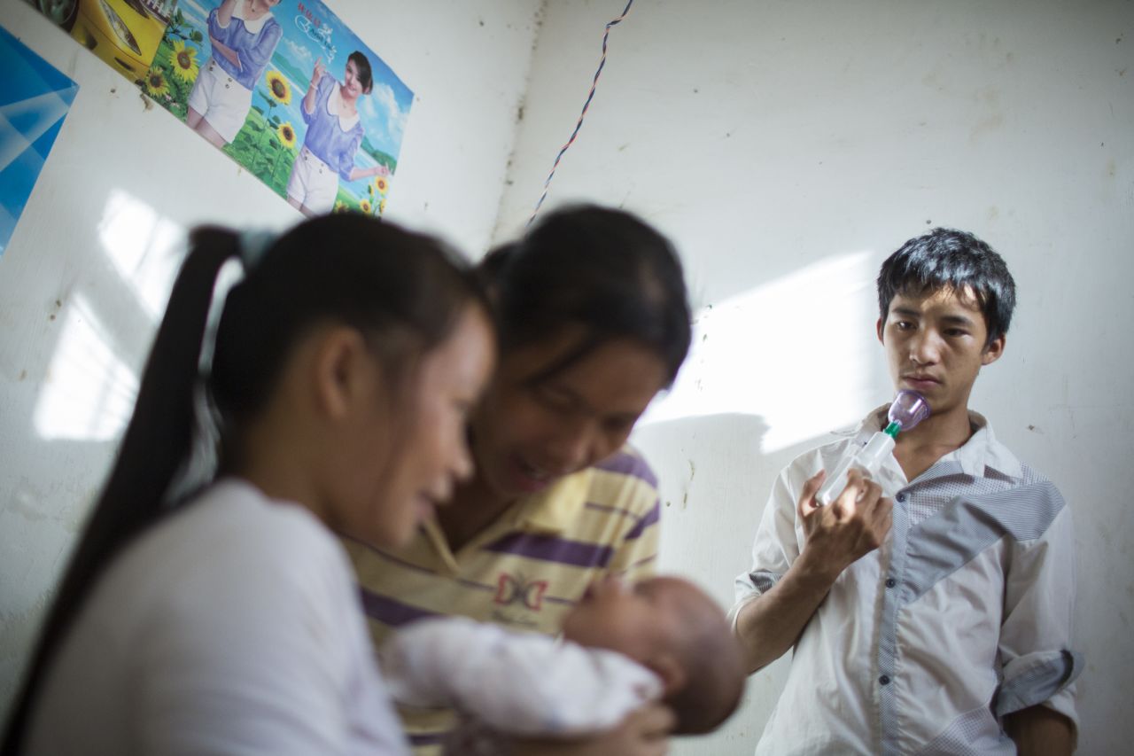 Ming holds a breast pump as he watches his wife, Cai, and his mother care for his newborn son. 