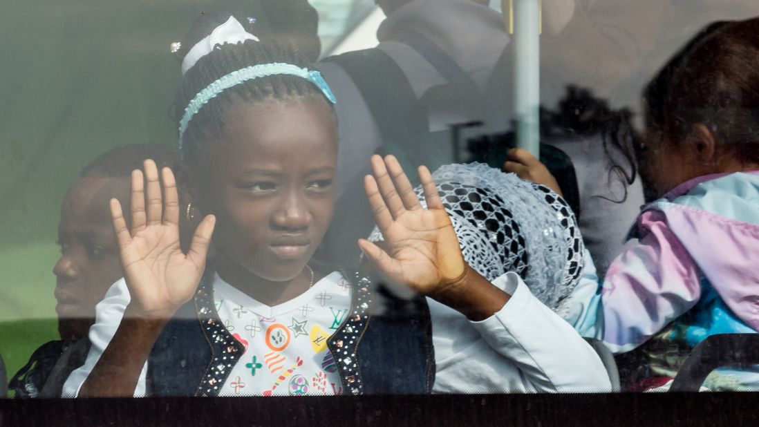 A young girl looks out of the window of a bus after airport evacuations.
