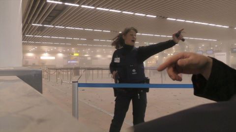 A police officer directs passengers in a smoke-filled airport terminal.