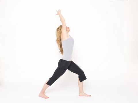 From standing, step your right foot back, as though coming into a lunge, but place your heel down with your toes angled slightly out. Bend your left knee to align above your ankle. Keep your back leg straight. Place your left hand on your left hip. If balance is a challenge, place your left hand on a wall or other support. Inhale as you reach your right arm overhead to the left, stretching your right side and front of your hip. Avoid arching your low back. Hold the stretch for a few breaths. Repeat on the opposite side.
