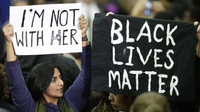 Kshama Sawant, left, a member of the Seattle City Council, a sign opposing Democratic presidential candidate Hillary Clinton next to another protester holding up a "Black Lives Matter" sign on Tuesday, March 22, following a campaign rally at Rainier Beach High School in Seattle.