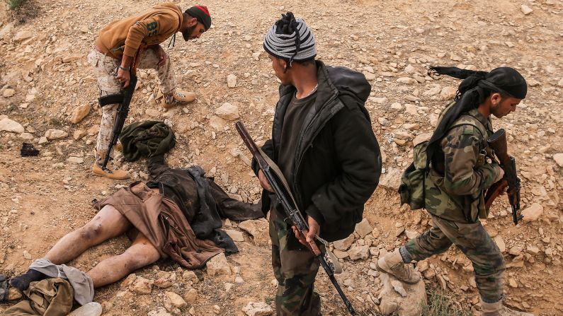 Syrian soldiers stand near the body of an ISIS militant near Palmyra on Friday, March 25.