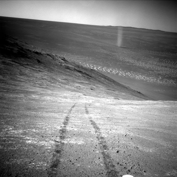 From its perch high on a ridge, Opportunity recorded this image of a Martian dust devil twisting through the valley below. Just as on Earth, a dust devil is created by a rising, rotating column of hot air. When the column whirls fast enough, it picks up tiny grains of dust from the ground, making the vortex visible.