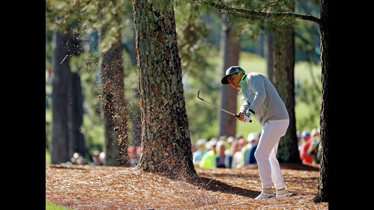 Rickie Fowler hits out of the trees near the first fairway.