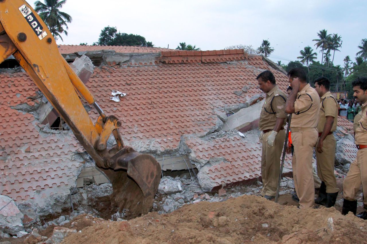 Indian officials look on as an excavator moves debris from a collapsed building.