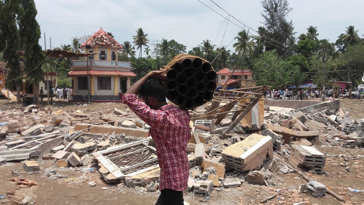A man carries empty shells of fireworks past a collapsed building  at the Puttingal temple complex.