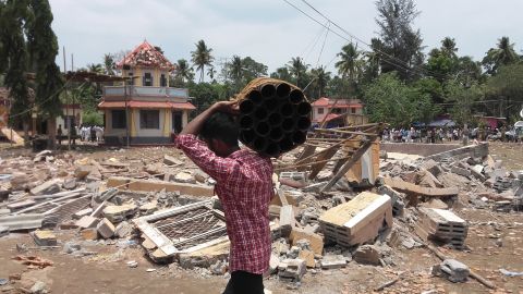 A man carries empty fireworks shells past a collapsed building after Sunday's temple fire