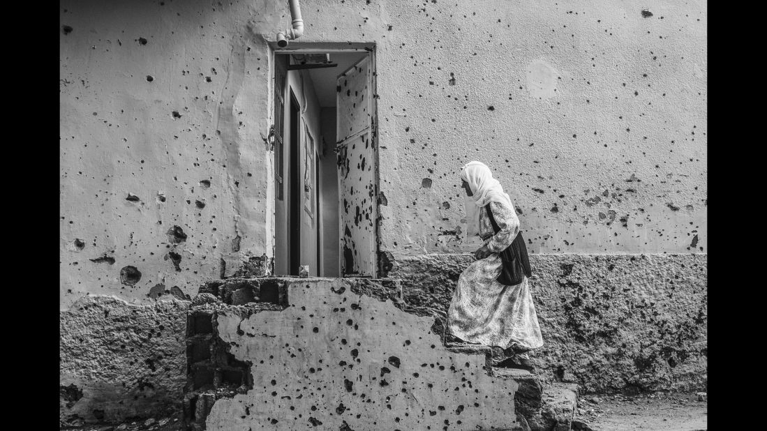A woman waits outside her house in Diyarbakir, Turkey, in October. The wall was riddled with bullet marks during clashes between Turkish armed forces and Kurdish rebels.