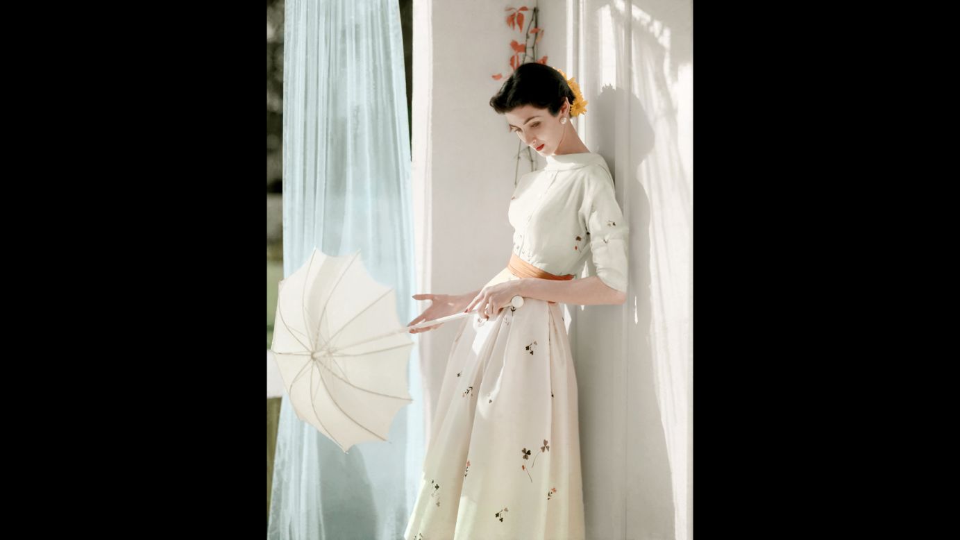 A model holds a parasol in her hands as she leans against a wall in 1953.