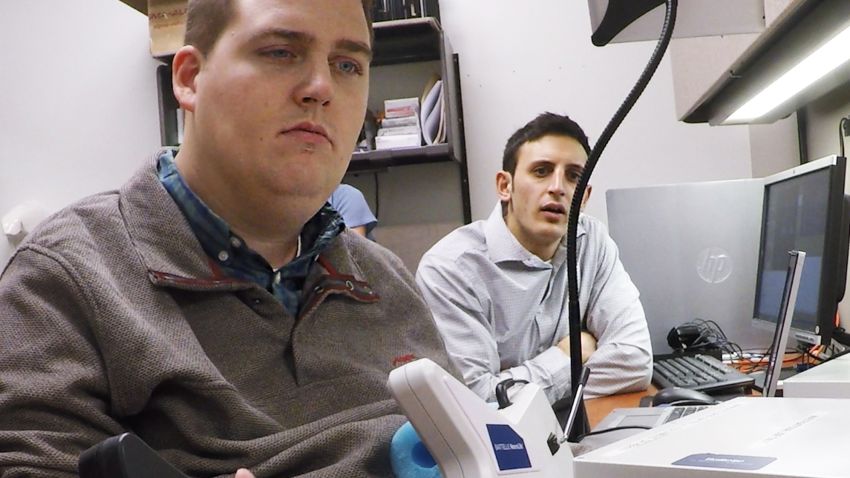 Nick Annetta, right, of Battelle, watches as Ian Burkhart, 24, plays a guitar video game using his paralyzed hand. A computer chip in Burkhart`s brain reads his thoughts, decodes them, then sends signals to a sleeve on his arm, that allows him to move his hand.