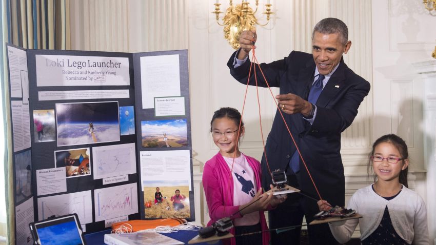 US President Barack Obama holds a homemade spacecraft that was attached to a weather balloon and launched 78,000 feet up into the atmosphere by 11-year-old Rebecca Yeung (L) and 9-year-old Kimberly Yeung (R) as he tours the 2016 White House Science Fair in the East Room at the White House in Washington, DC, April 13, 2016. / AFP PHOTO / SAUL LOEBSAUL LOEB/AFP/Getty Images
