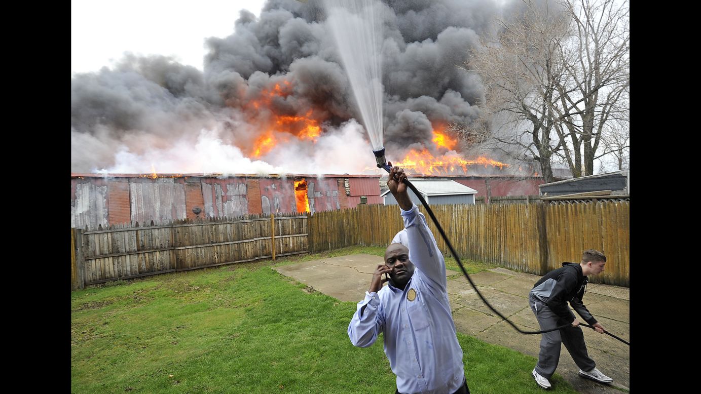 A man in Erie, Pennsylvania, uses a garden hose to wet the side of his house as a warehouse fire rages behind him on Monday, April 11.