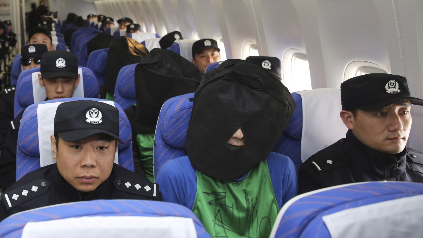 Suspects accused of wire fraud are guarded on a plane as they arrive in Beijing on Wednesday, April 13.