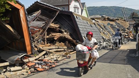 A woman rides a scooter in front of a collapsed house in Mashiki on April 15.