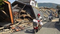 A woman rides a scooter in front of a collapsed house a day after the Kumamoto Earthquake on April 15 in Mashiki, Japan.