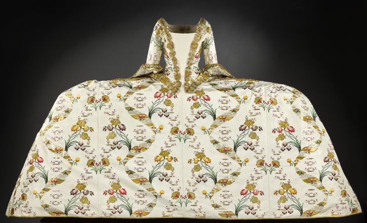 The mantua was worn for court occasions and was designed to be a luxurious garment, often decorated with opulent embroidery incorporating gold or silver thread, to display status and wealth. This example, brocaded in gold and trimmed with gilt lace, is thought to have belonged to the Countess of Haddington. <br /><br />It is particularly interesting to the contemporary eye not only for its extravagance -- the fabric alone would cost the equivalent of around £5,000 ($7,200) today -- but for its sheer enormity. 