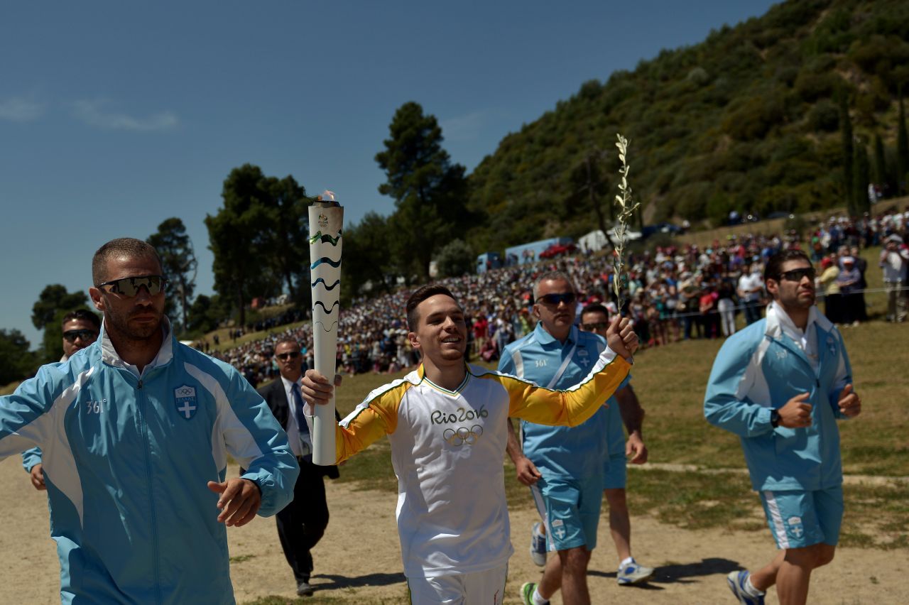 The first torchbearer was Greek gymnastics world champion Eleftherios Petrounias. The torch is beginning a six-day relay tour of Greece which includes a pass through a refugee camp in Athens.