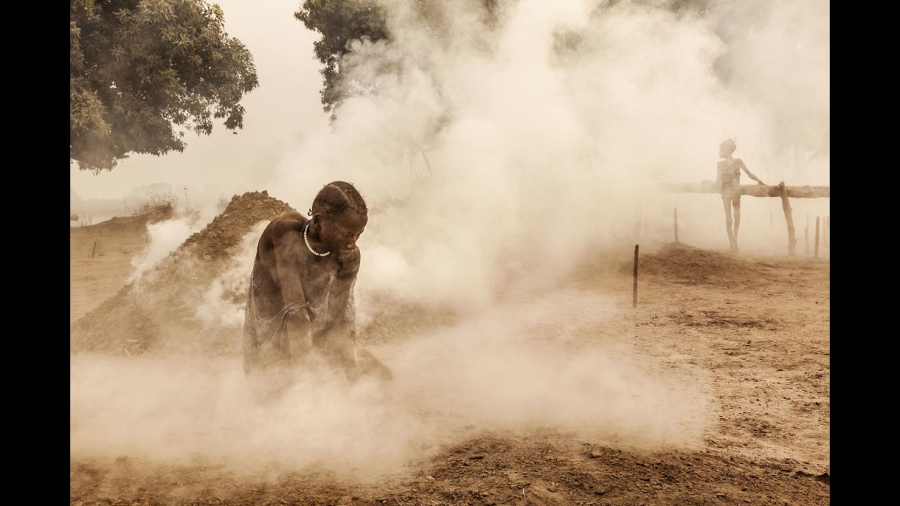 A Mundari woman clears the ground of sticks and dung before the cattle return home from the pastures. Women also milk the animals and look after the children.
