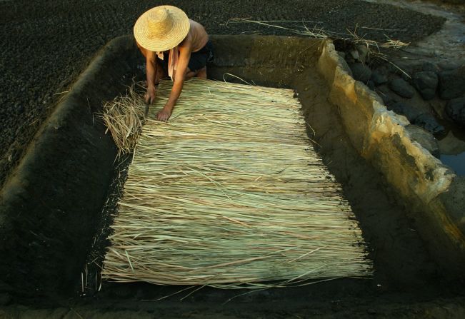 A Chinese man in a fishing village prepares straw and bamboo mats to be used for creating thick brine which is then turned into salt. 
