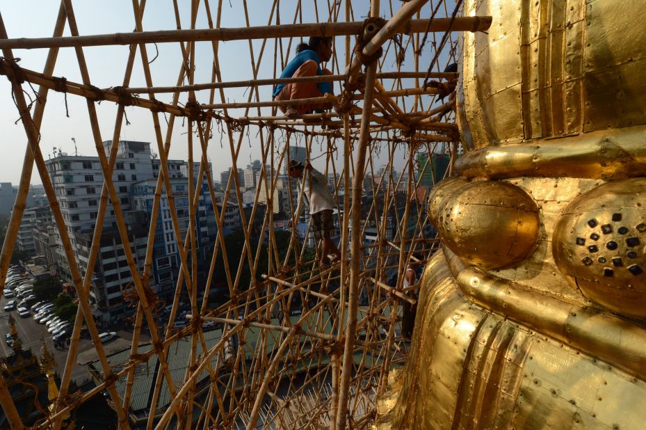 Myanmar craftsmen dismantle bamboo scaffolding on a section of the Sule Pagoda tower after installing gold covering and decorating it with gemstones.