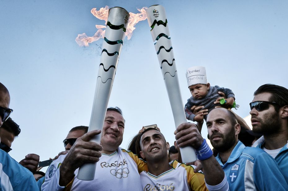 In a show of solidarity, president of the Hellenic Olympic Committee, Spyros Kapralos (L),  passed the Olympic Flame to a Syrian refugee, Ibrahim al-Hussein at the Eleonas refugee camp in Athens Tuesday.