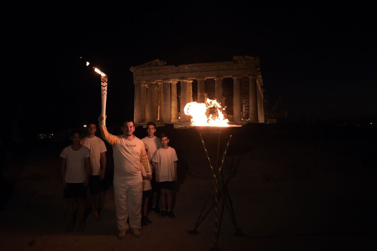 Greek former Olympic weightlifting gold medalist Pyros Dimas also held the torch, and stands here atop the Acropolis hill by the the ancient temple of the Parthenon, after lighting a cauldron with the Olympic flame. 